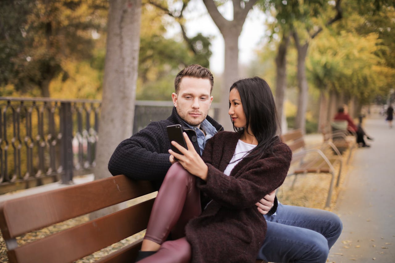 Couple sitting on a bench using a smartphone on a beautiful fall day.