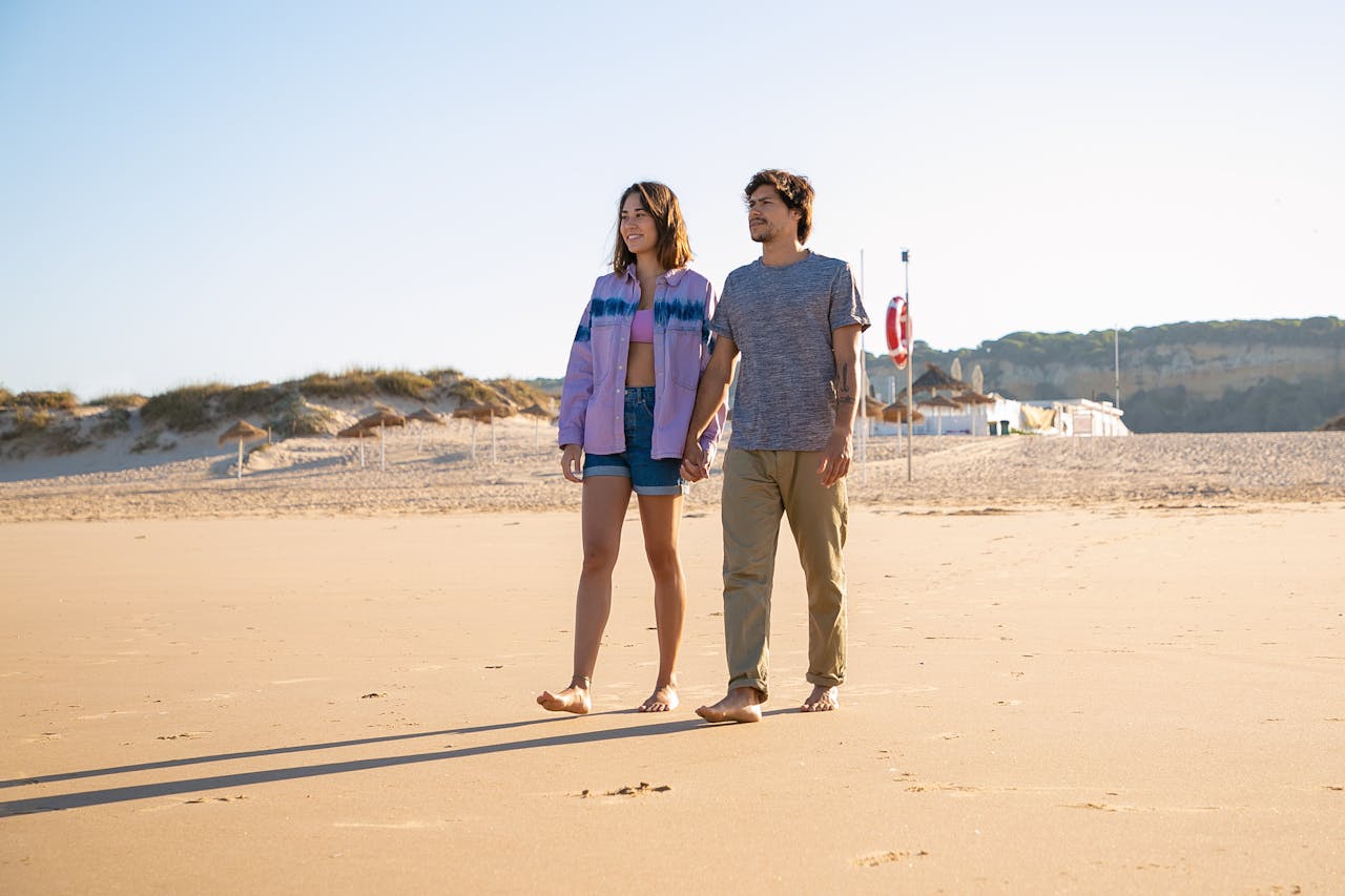 A happy couple walking barefoot on a sunlit beach in Portugal, enjoying a leisure day.